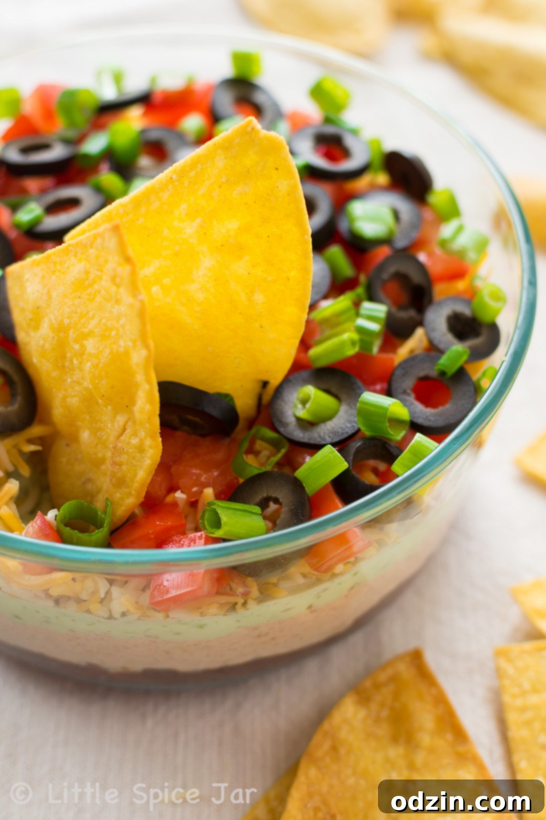 seven layer dip on glass bowl surrounded by homemade tortilla chips