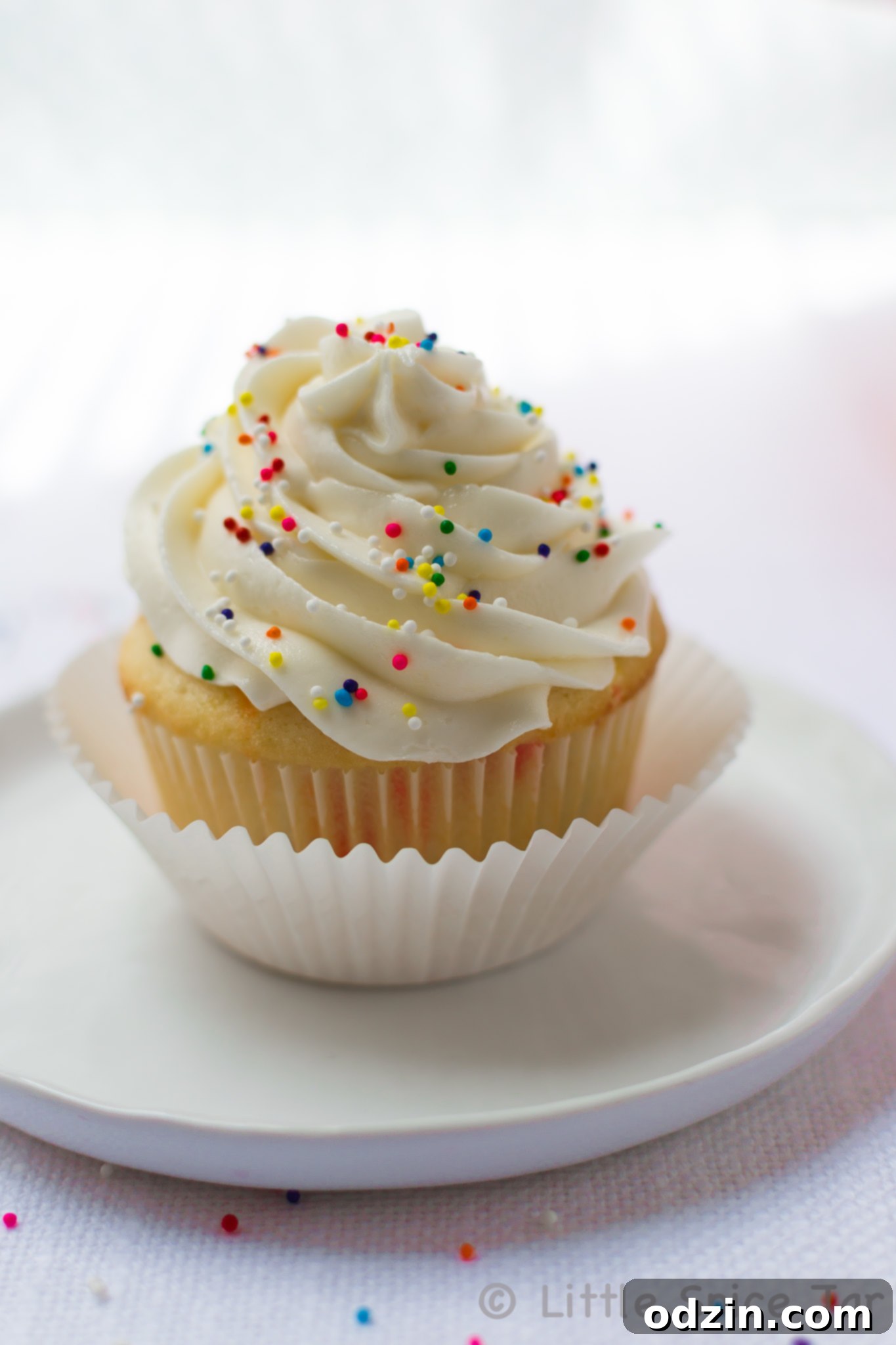 prepared funfetti cupcake with whipped topping and sprinkles on white plate on white surface