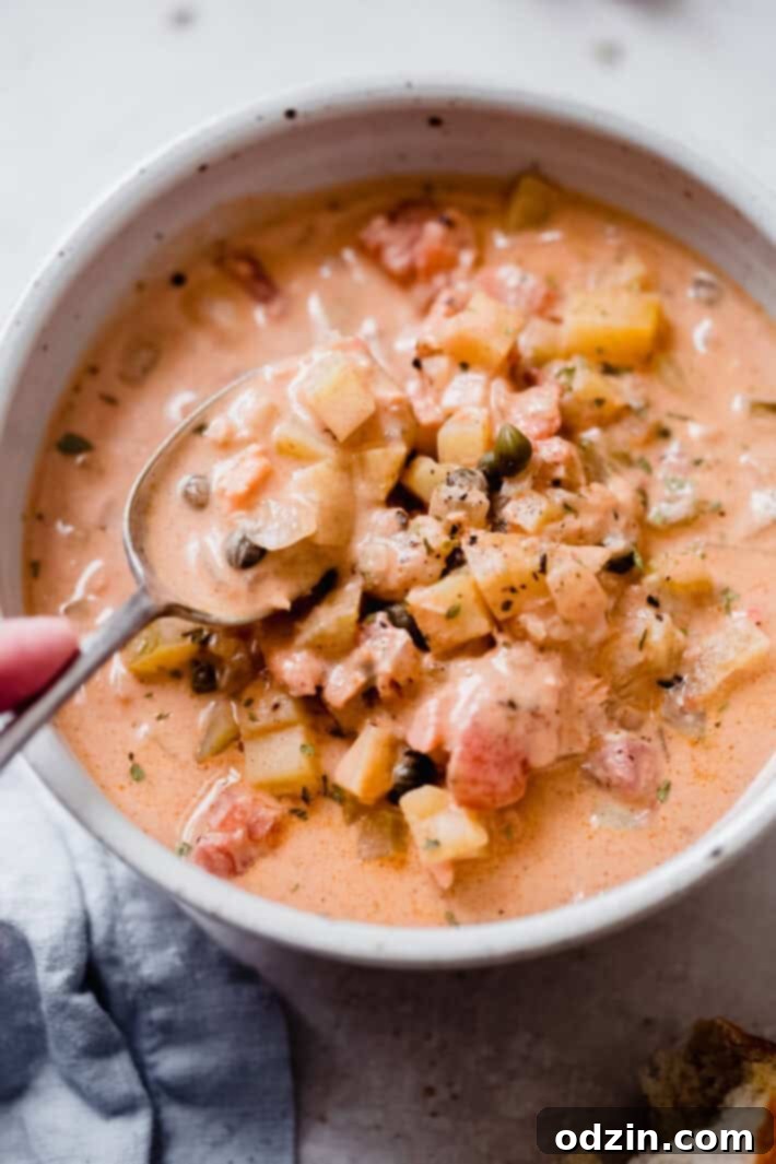 hand lifting spoonful of chowder from speckled bowl