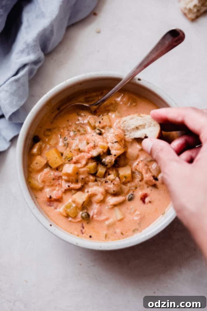 hand dipping a piece of bread into a bowl of chowder