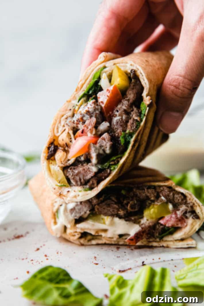 Close-up of a beef shawarma sandwich, cut in half and stacked, with a hand holding a portion