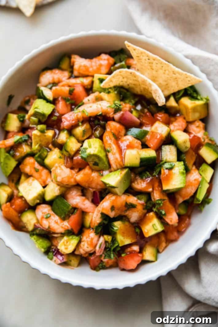Prepared Mexican shrimp cocktail with vibrant vegetables served in a bowl alongside tortilla chips.