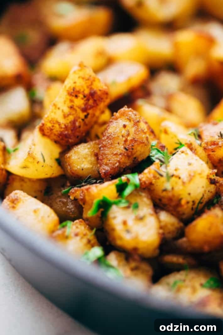 Close up of crispy coated cubes of potatoes pan-fried in a cast iron skillet, showcasing their irresistibly golden brown texture and seasoned crust