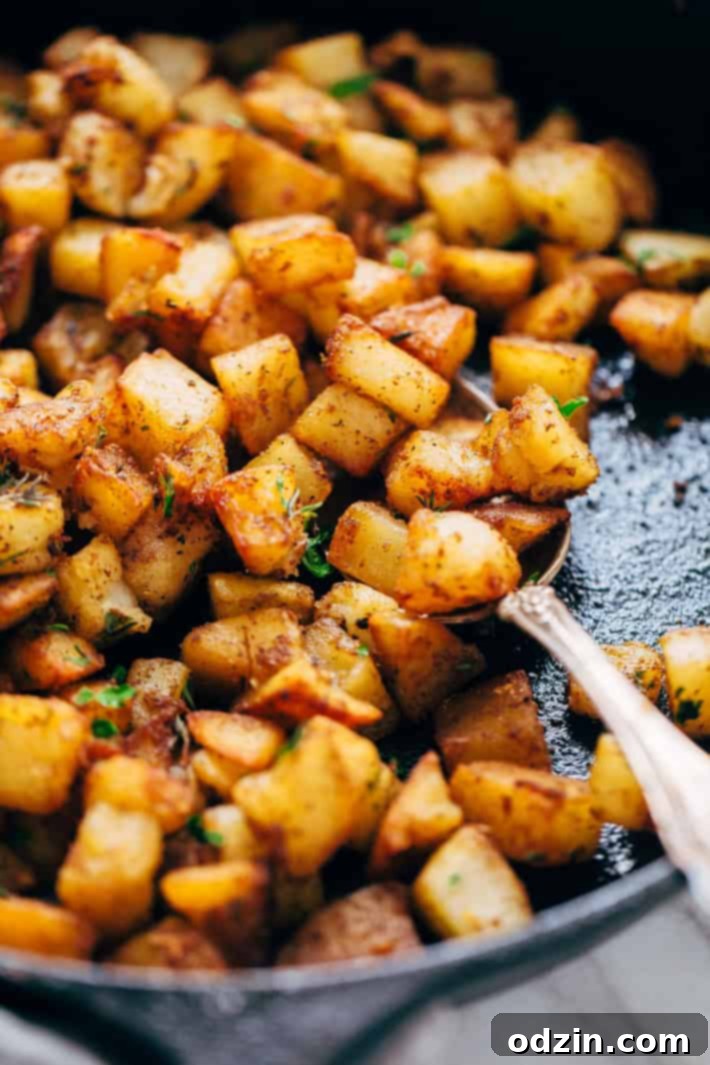 Cast iron skillet filled with perfectly seasoned and fried breakfast potatoes, with a spoon scooping a portion, highlighting their crispiness