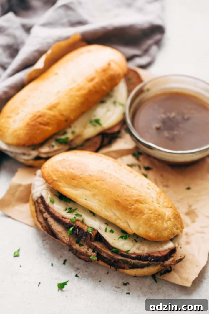 Finished Slow Cooker French Dip sandwich, cut in half, with a bowl of au jus and a rustic backdrop.