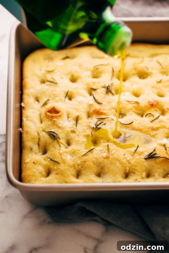 olive oil being drizzled over warm focaccia bread in baking pan