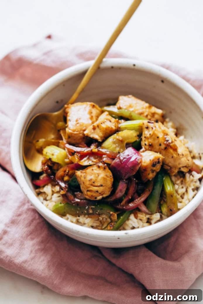 bowl of brown rice topped with chicken and vegetable stir fry on mauve linen napkin
