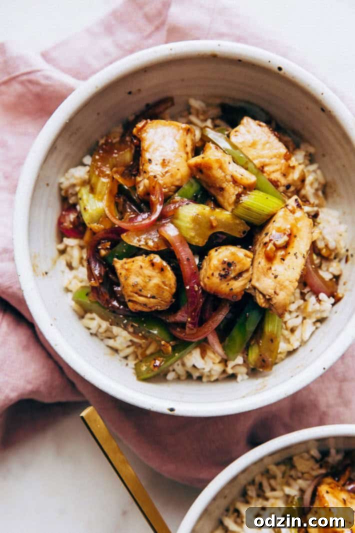 top shot of speckled bowl holding brown rice topped with sautéed vegetables and chicken stir fry on mauve linen napkin with gold spoon