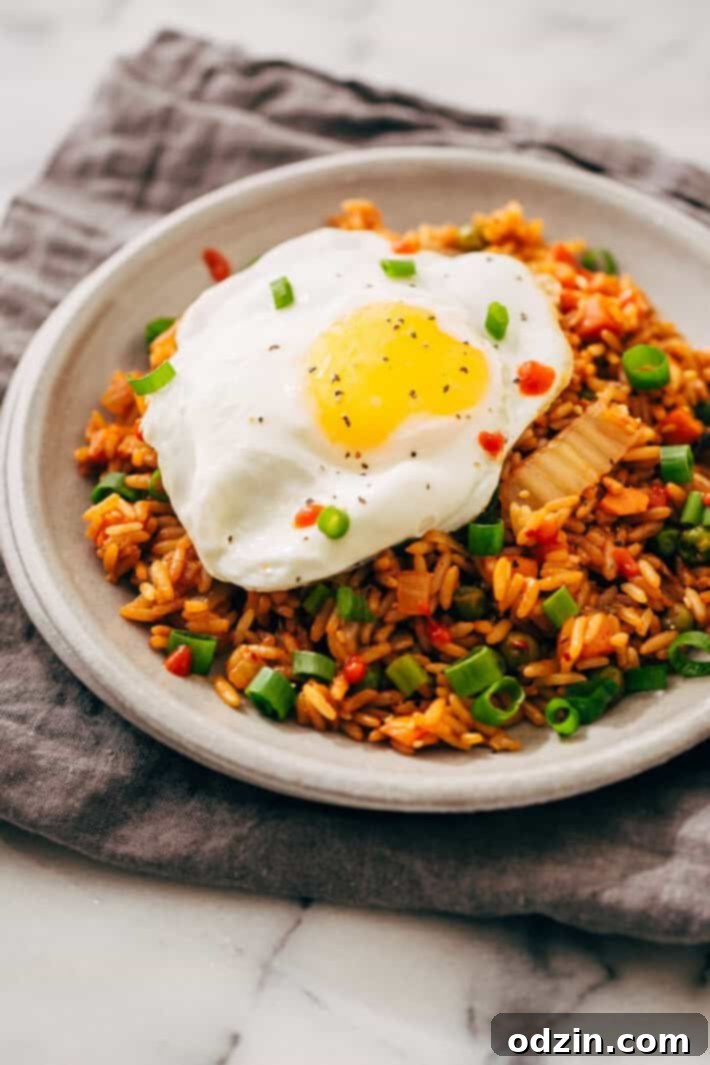 Quick Kimchi Fried Rice - Easy Recipe with Leftover Rice A close-up shot of delicious kimchi fried rice in a pan, featuring vibrant red kimchi, rice, and green onions.