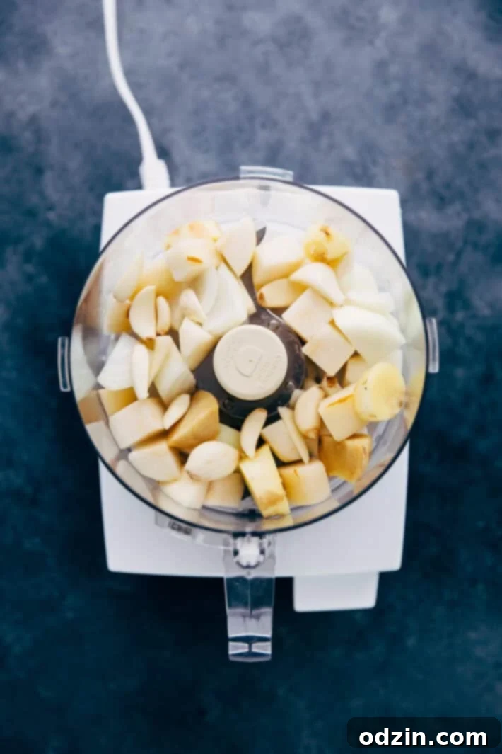 A food processor bowl containing chopped pears, yellow onion, garlic cloves, and fresh ginger, ready to be blended into a savory paste for the Korean beef marinade.