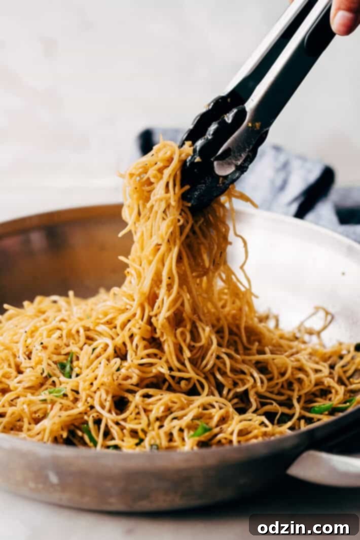 Tongs lifting a portion of hot garlic noodles from a pan, ready to be served
