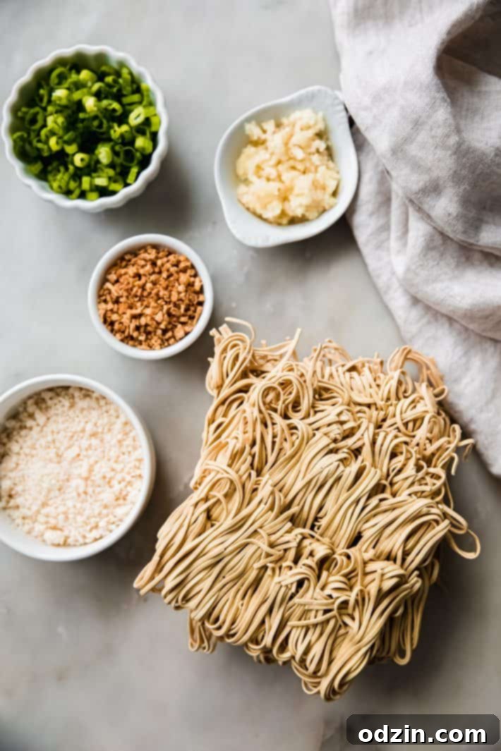 Assorted ingredients for garlic noodles laid out on a white marble surface, including garlic, scallions, sauces, and cheese
