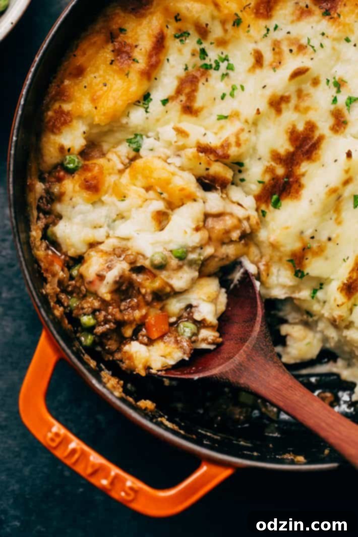 Classic shepherd's pie in a cast iron dish with a serving spoon, showcasing its bubbly, cheesy crust