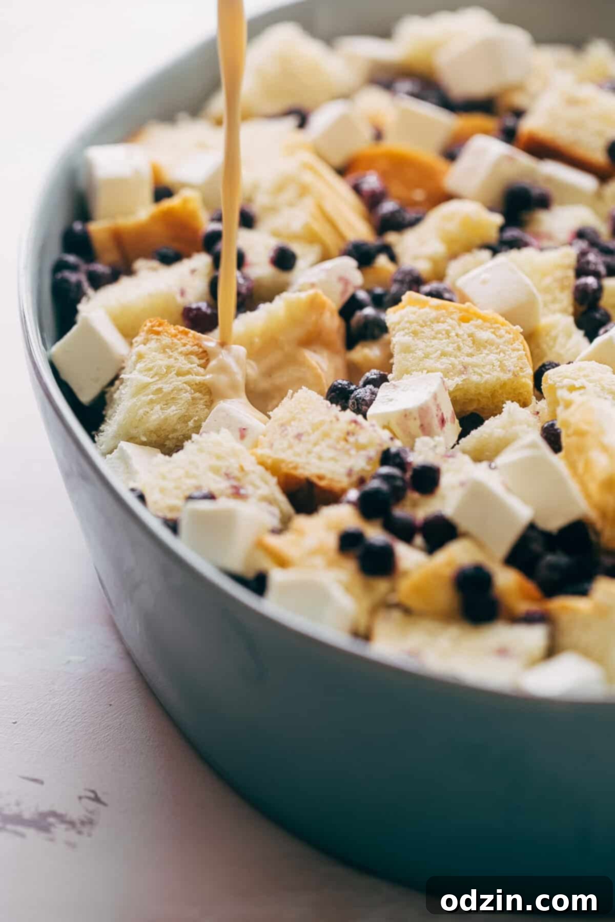 pouring egg batter into bowl with bread, cream cheese, and frozen blueberries 