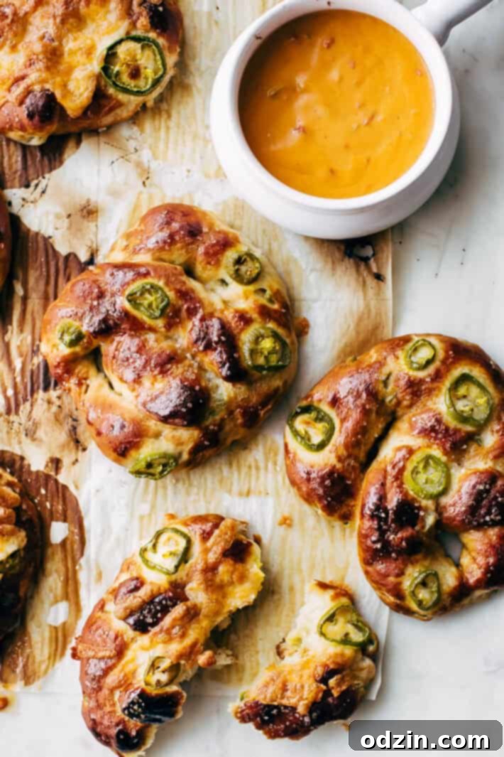 Freshly baked homemade Cheddar Jalapeño Soft Pretzels on a baking sheet, loaded with cheese and pickled jalapeños.