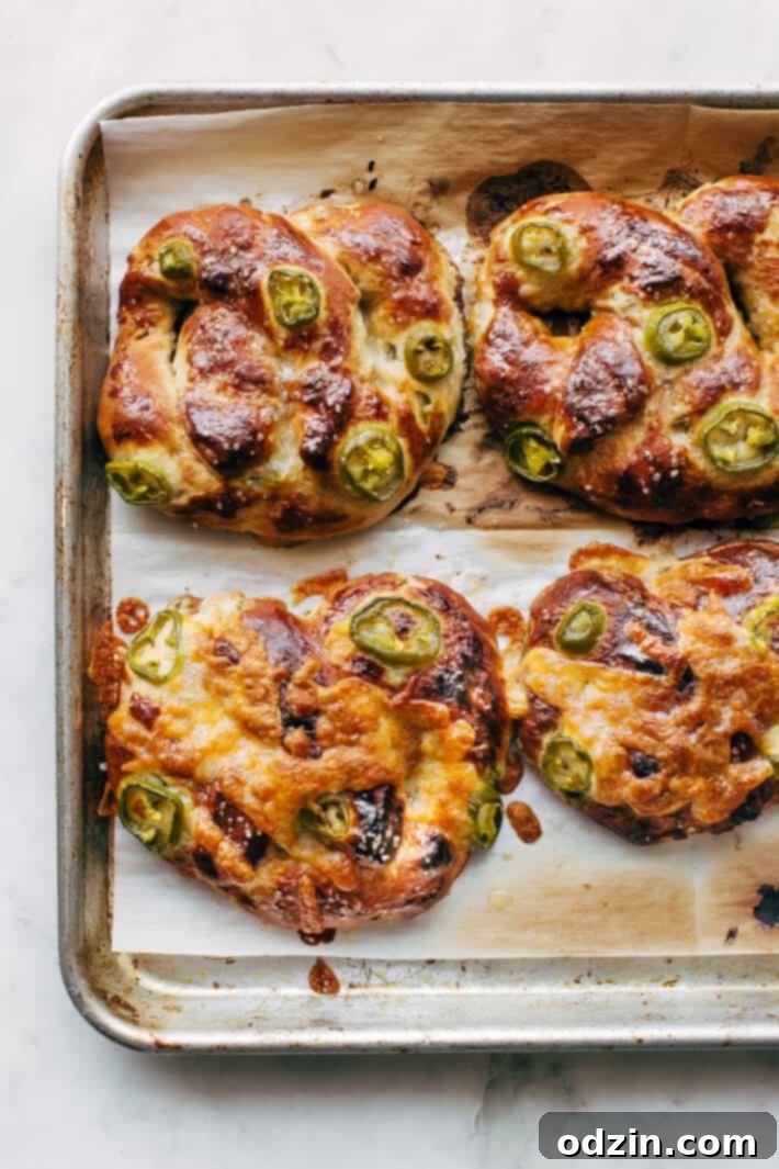 Two hands holding a fresh Cheddar Jalapeño Soft Pretzel with melted cheese.