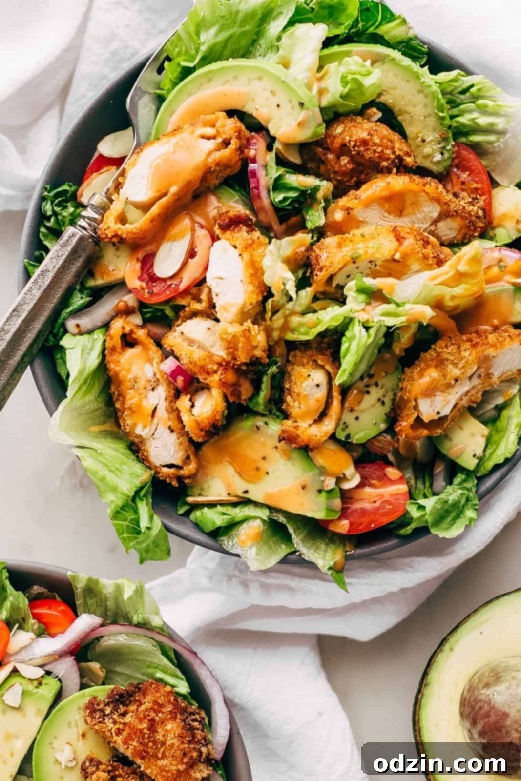bowls of romaine topped with avocado slices, red onions, crispy chicken strips, almonds, and grape tomatoes