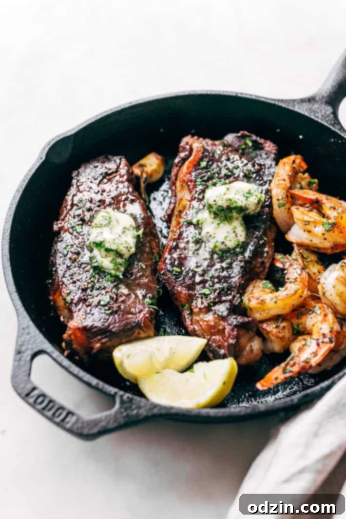 Close-up of golden-brown garlic butter steak and pink cooked shrimp in a cast iron skillet, garnished with fresh rosemary.