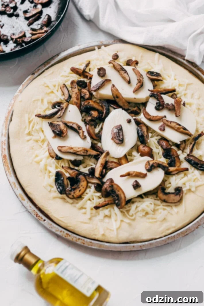 Ingredients for Homemade Truffled Mushroom Pizza laid out on a wooden surface: fresh cremini and shiitake mushrooms, shredded fontina, fresh mozzarella, and a bottle of white truffle oil. A simple yet elegant recipe for pizza lovers.