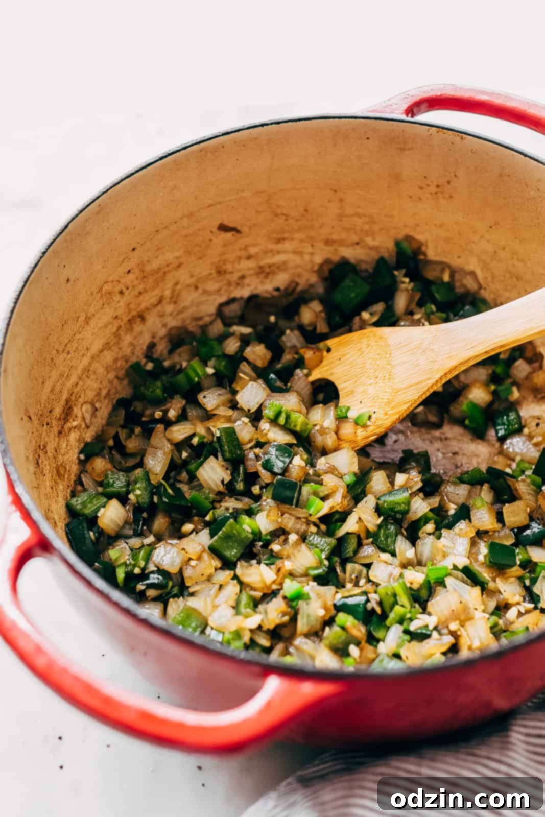 sautéed diced poblano peppers nad onions in cast iron pot with wooden spoon