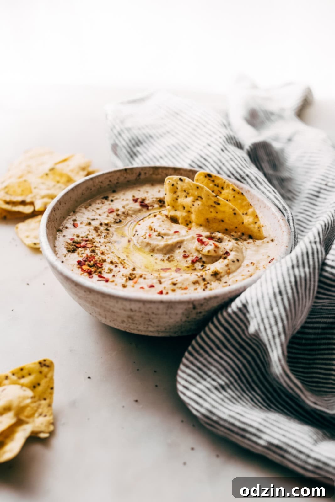 bowl of hummus on white marble with striped towel 