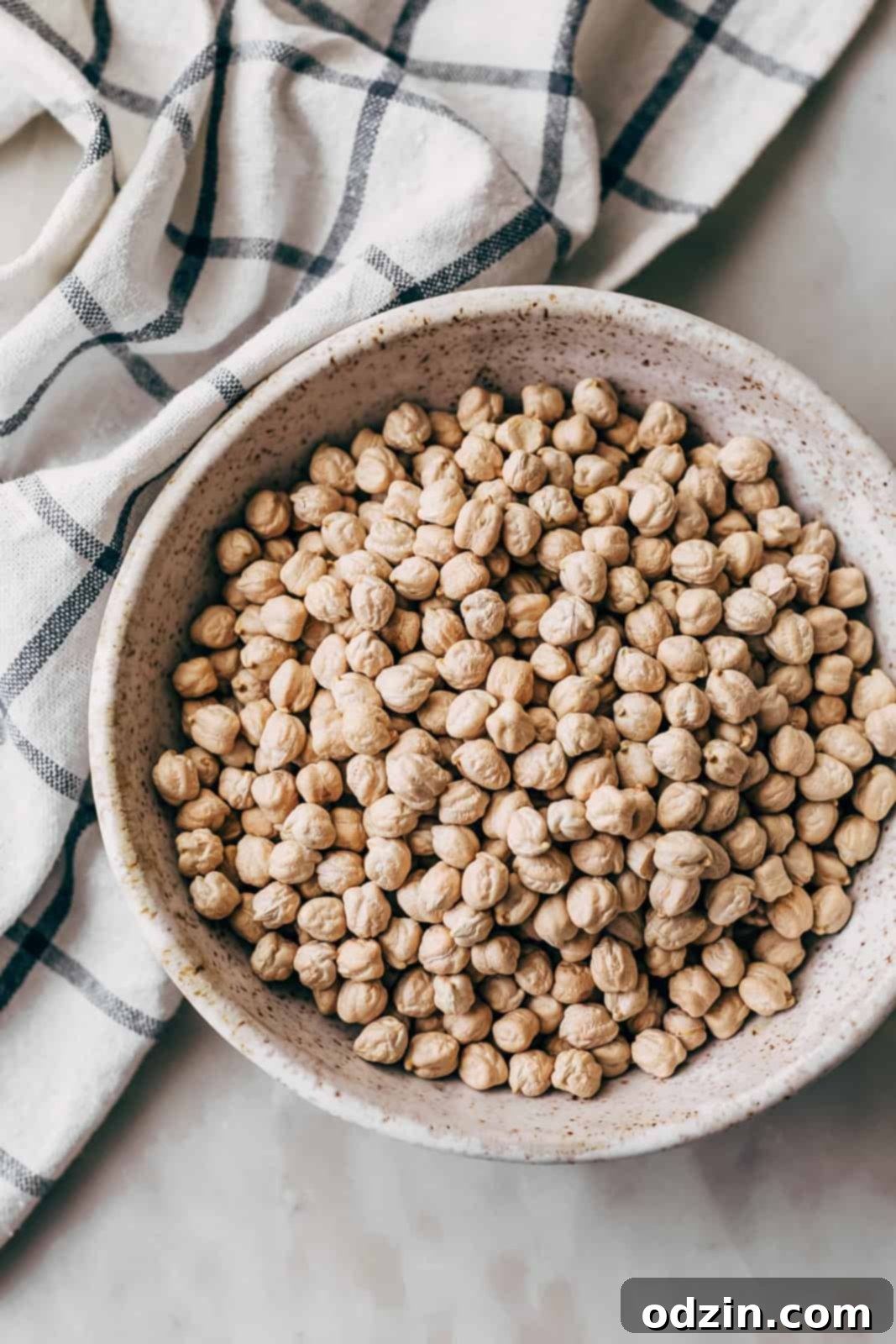 dry garbanzo beans in speckled bowl on white marble surface