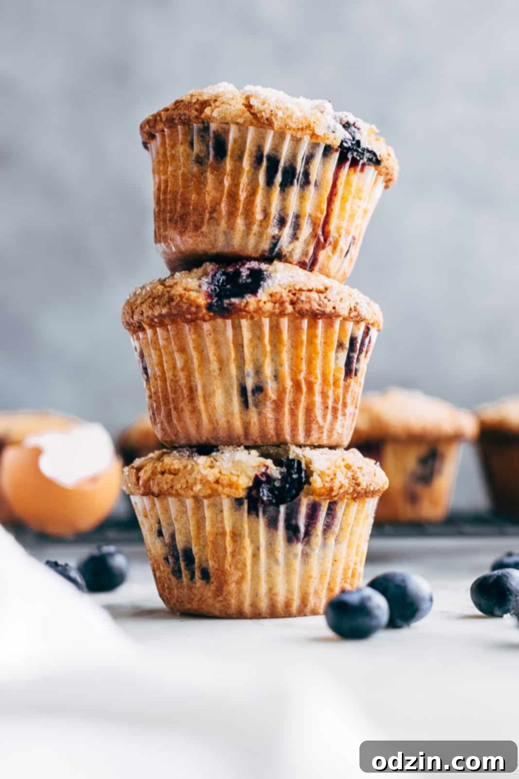 a tower of gluten-free blueberry muffins on white marble surrounded by muffins in the back
