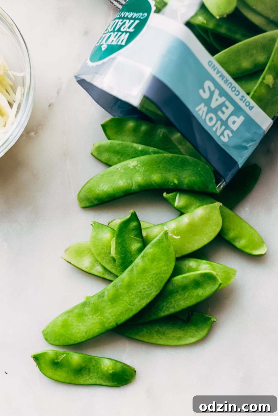 Speedy Ginger Shrimp and Snow Pea Stir Fry 4 crisp snow peas spilling out of a grocery bag onto a white marble surface, highlighting freshness
