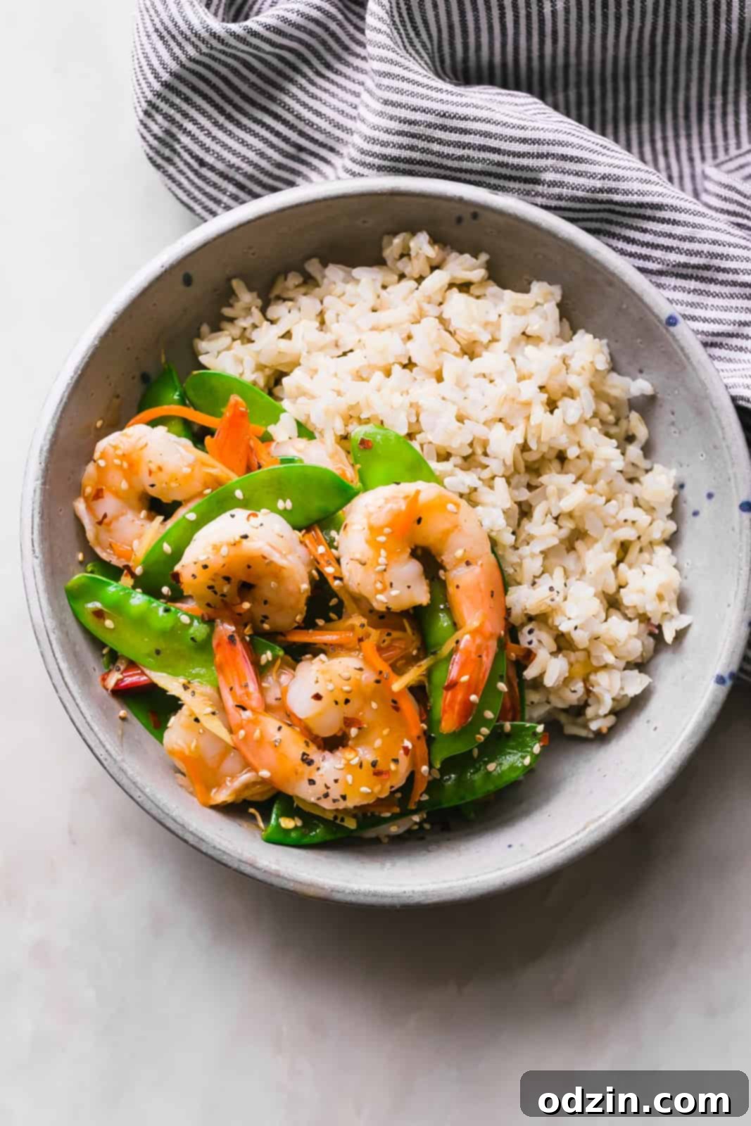 Speedy Ginger Shrimp and Snow Pea Stir Fry 6 cooked brown rice in a speckled bowl on one side, and the shrimp snow pea stir fry on the other, artfully arranged
