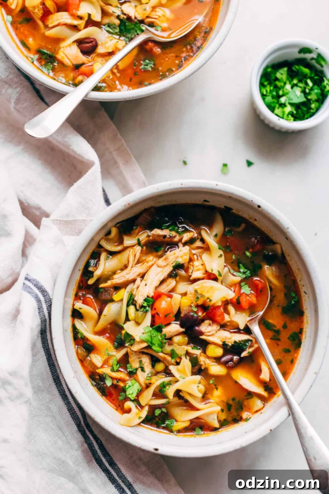 Multiple bowls of Mexican chicken noodle soup, with spoons resting in them, arranged invitingly on a white marble surface, ready to be enjoyed.