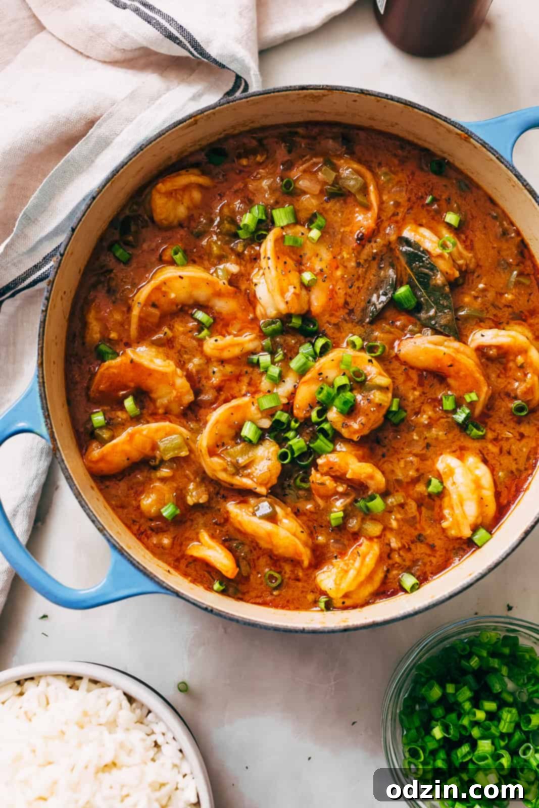 Spicy Cajun Shrimp Etouffee 4 cast iron pot with étouffée topped with scallions on white marble