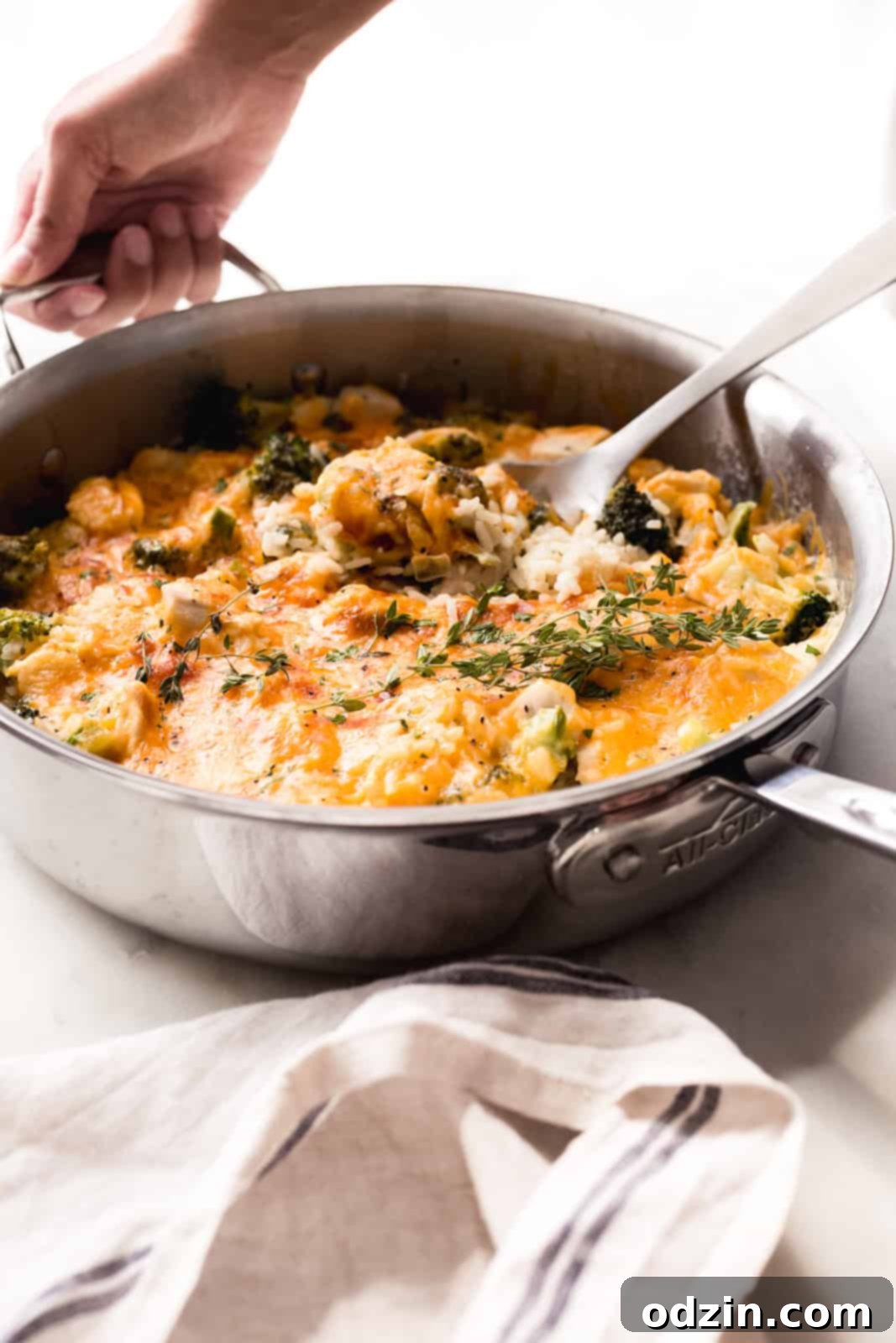 Easy One-Pot Cheesy Chicken, Broccoli & Rice Dinner 3 hand placing skillet down on white marble with casserole and spoon