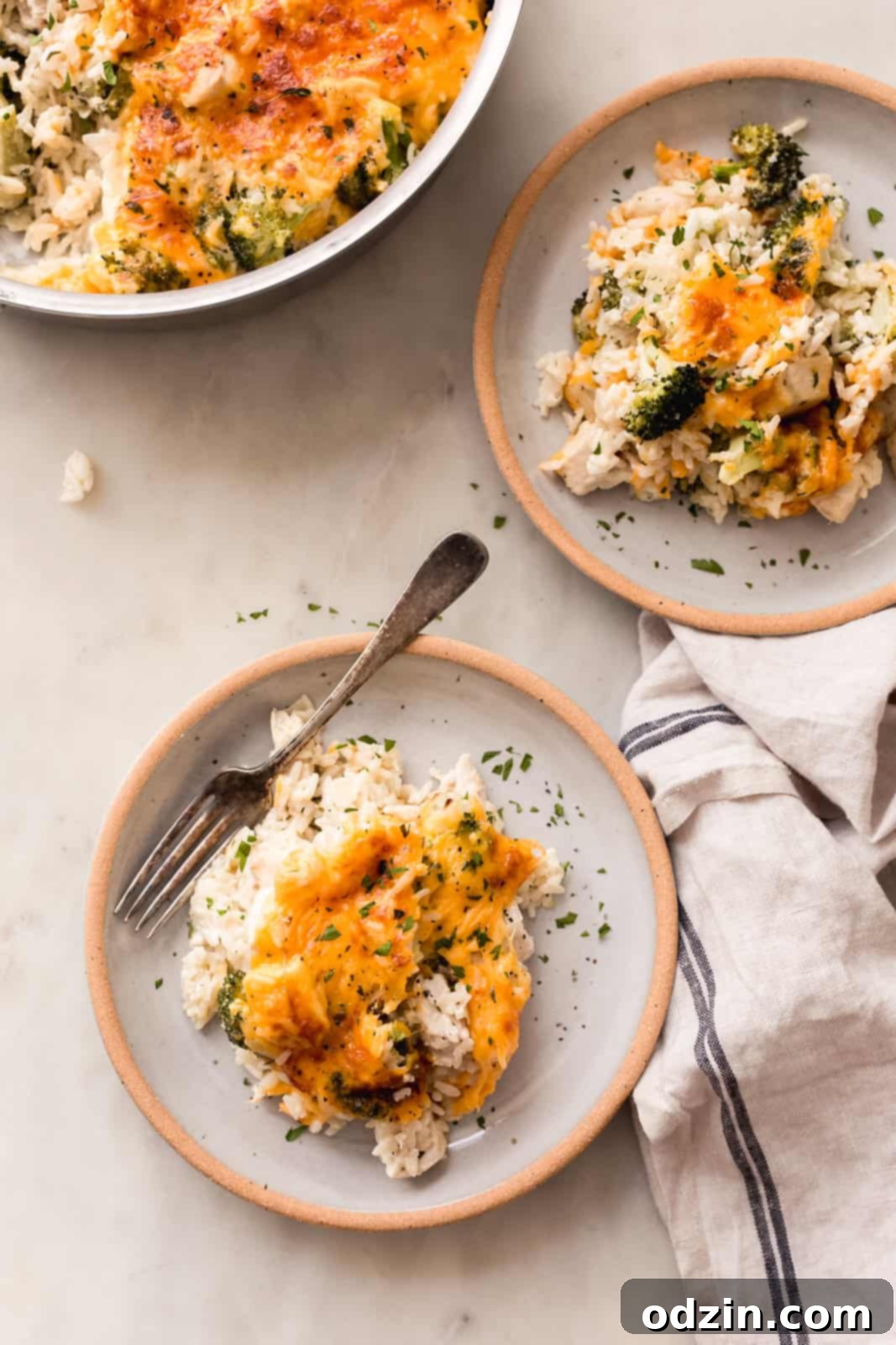 Easy One-Pot Cheesy Chicken, Broccoli & Rice Dinner 8 food scene with filled pan and plates of casserole on white marble