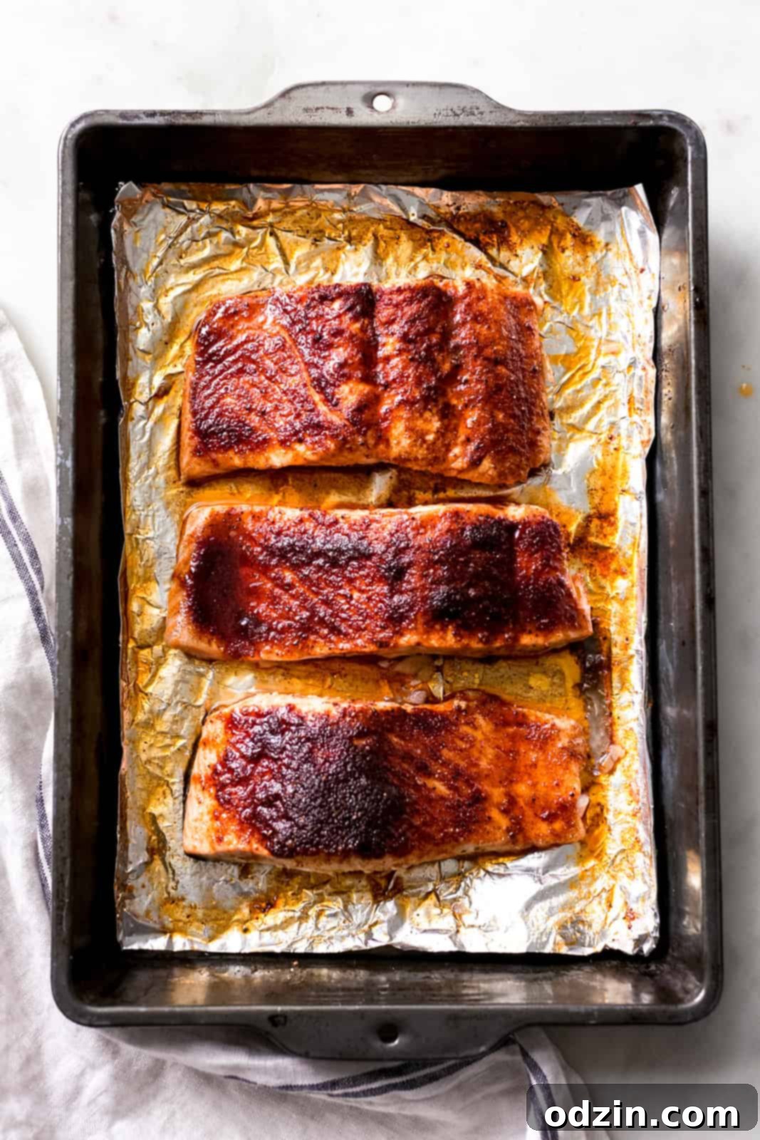 Multiple portions of maple glazed salmon on foil in a metal baking pan, ready for the oven.