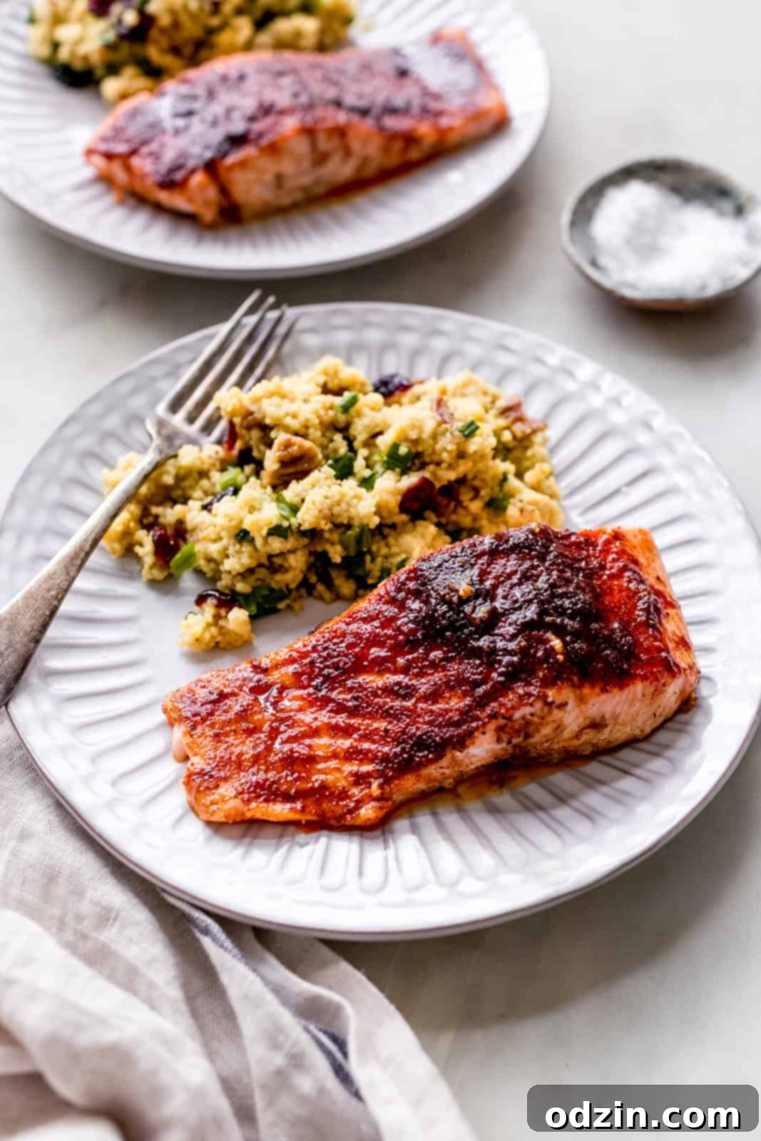 Fluted white plate with a blackened salmon fillet, curry couscous salad, and a fork, showcasing a delicious meal.
