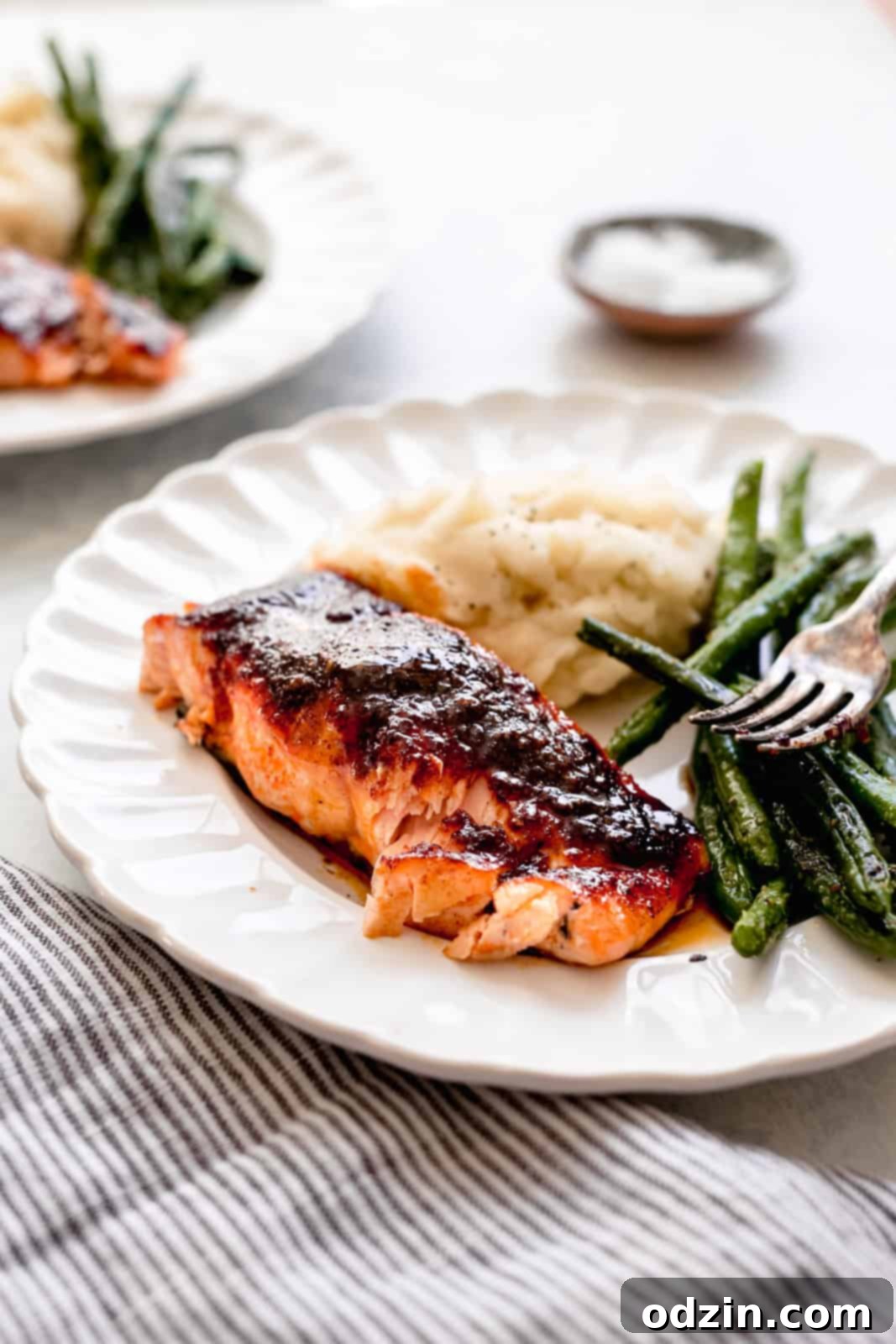 Flaked portion of spicy maple glazed salmon on a fluted white plate with sautéed green beans and a scoop of mashed potatoes, showcasing its perfect doneness.