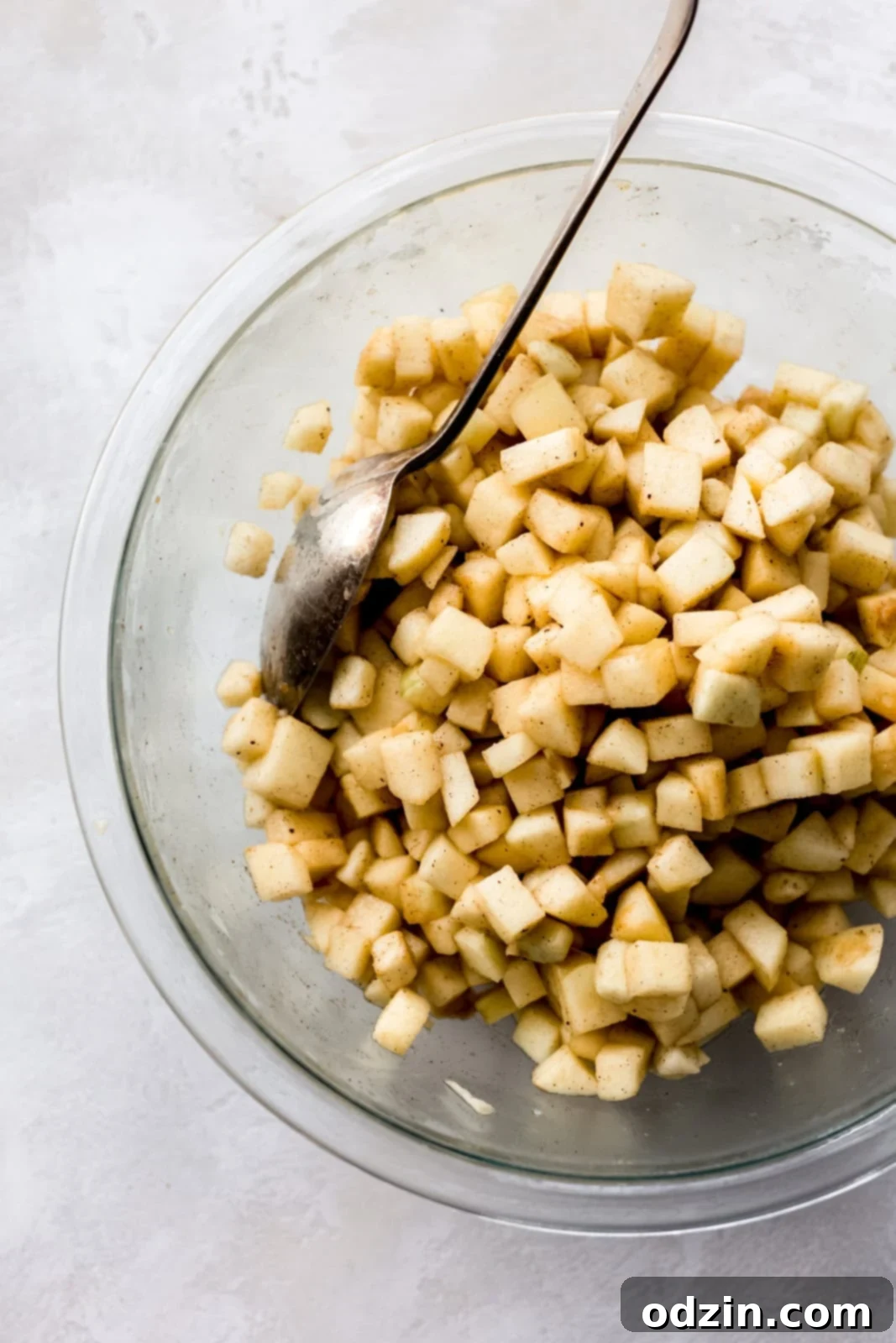 Golden Apple Crumble Bars 4 diced apples tossed with cinnamon in clear bowl with a spoon on grey surface