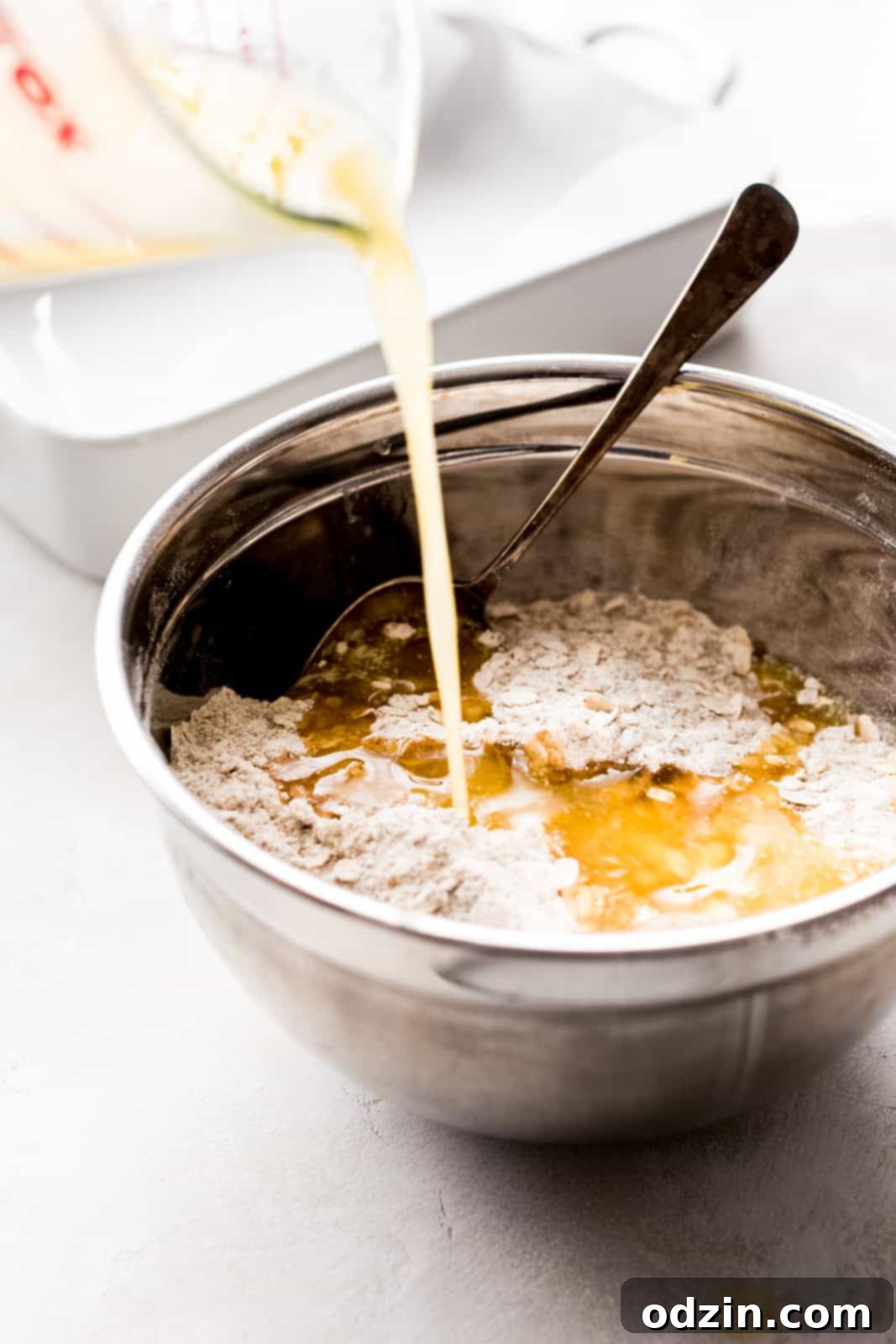 Golden Apple Crumble Bars 5 pouring melted butter to make crumble mixture in steel bowl with spoon