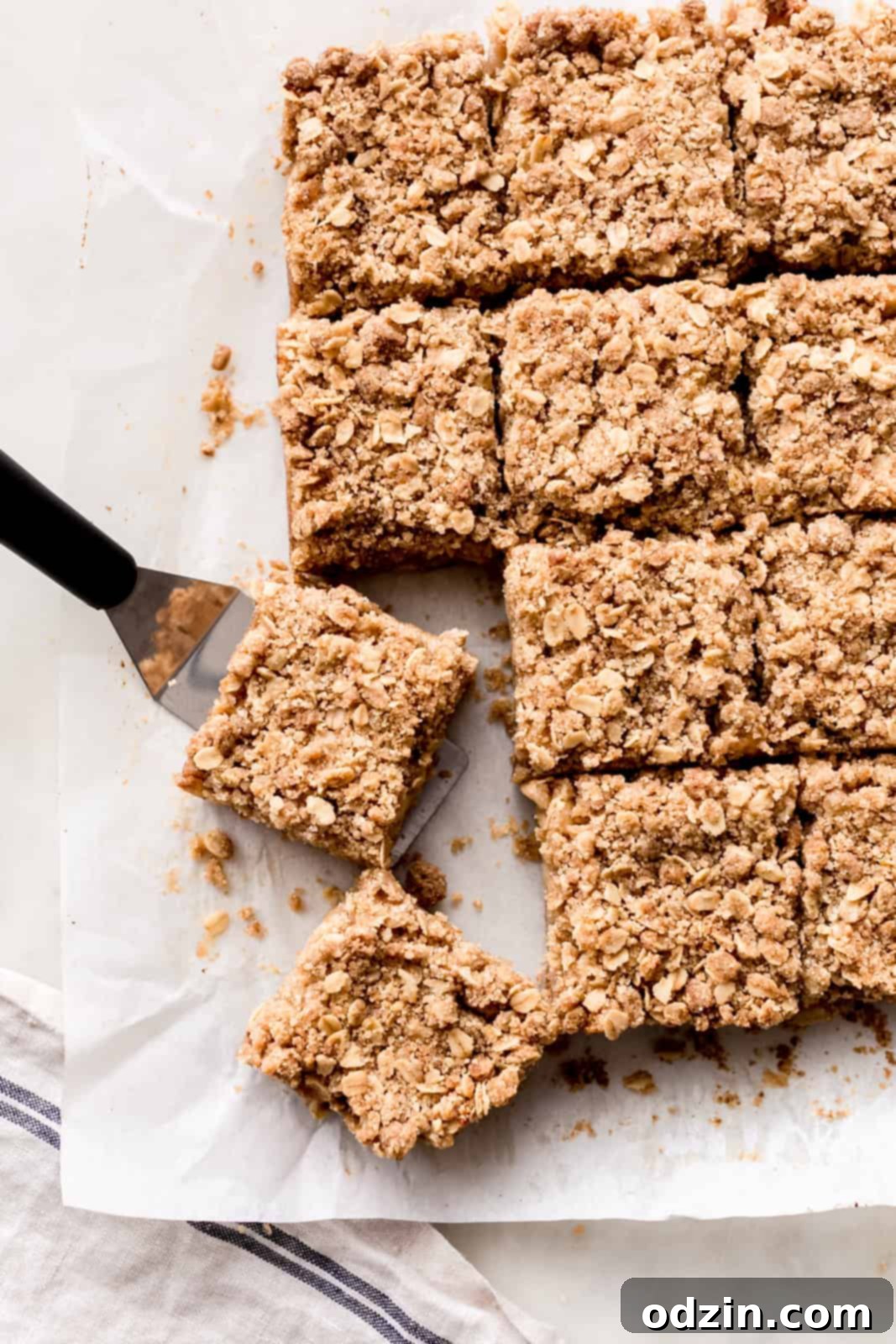 Golden Apple Crumble Bars 10 cut bars on white parchment with one piece on spatula