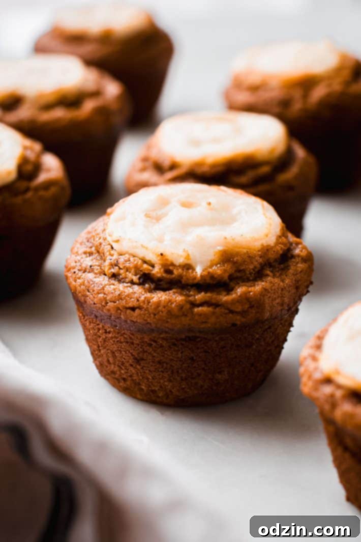 Chai-Spiced Pumpkin Cream Cheese Muffins 3 Close-up of a single chai pumpkin cheesecake muffin with a visible cheesecake swirl on a white marble surface.