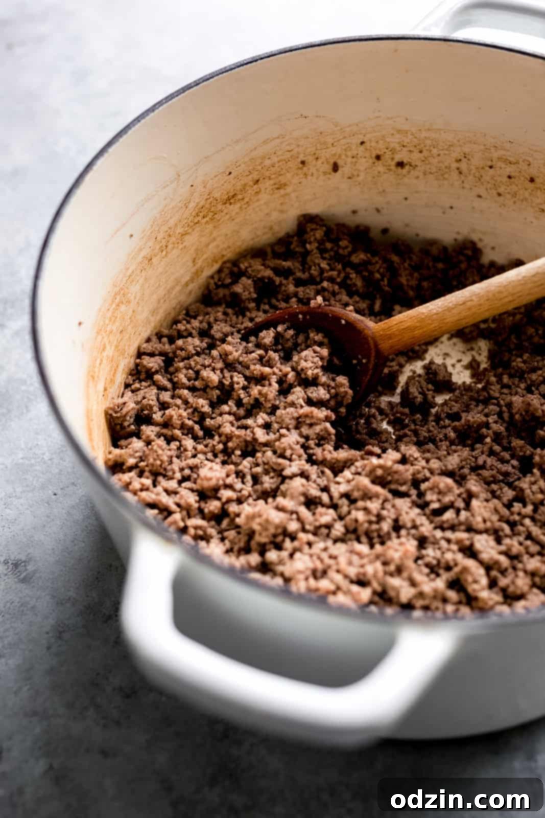 browned beef in cast iron pot with wooden spoon on grey surface