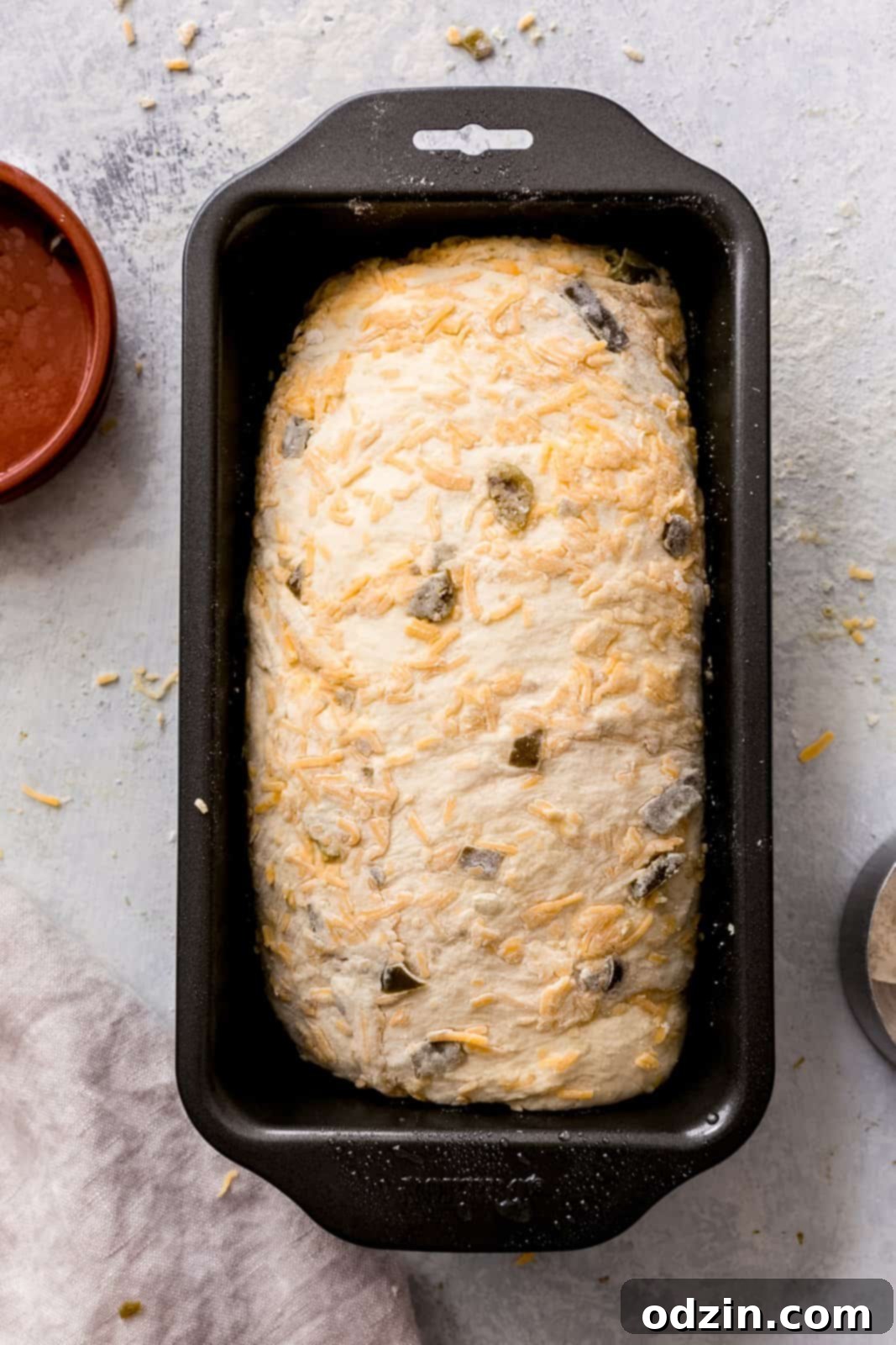 Spicy Cheddar Jalapeño Loaf 10 raw bread dough in loaf pan speckled with cheese on top before baking