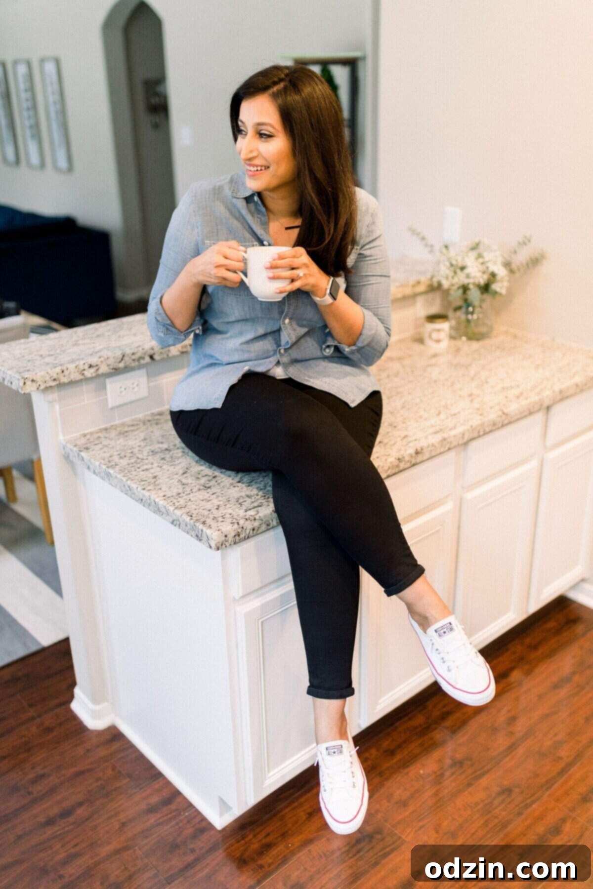 Author holding a warm coffee mug, deep in thought, sitting casually on a clean countertop in a bright kitchen.
