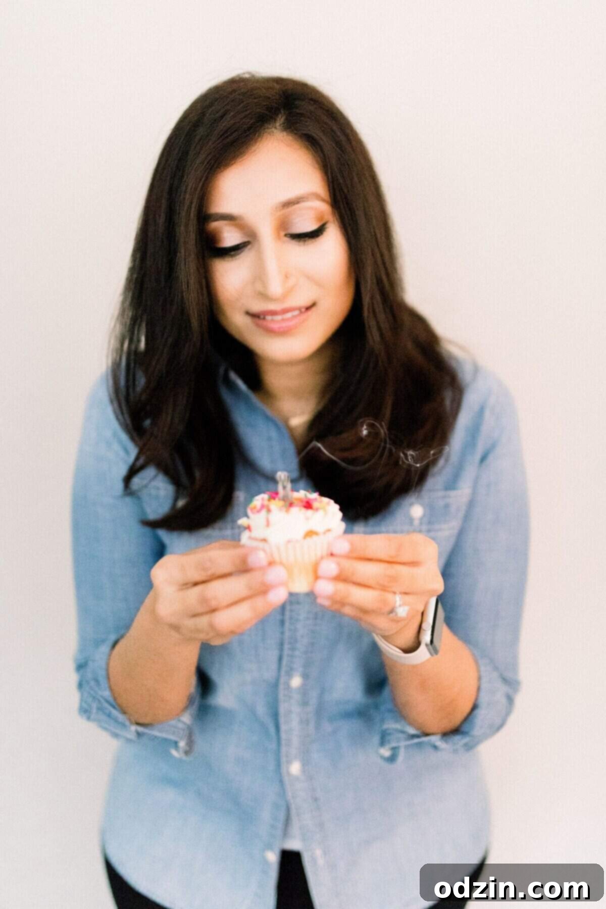 The author holding a festive cupcake with a recently blown-out candle, looking joyful and content.