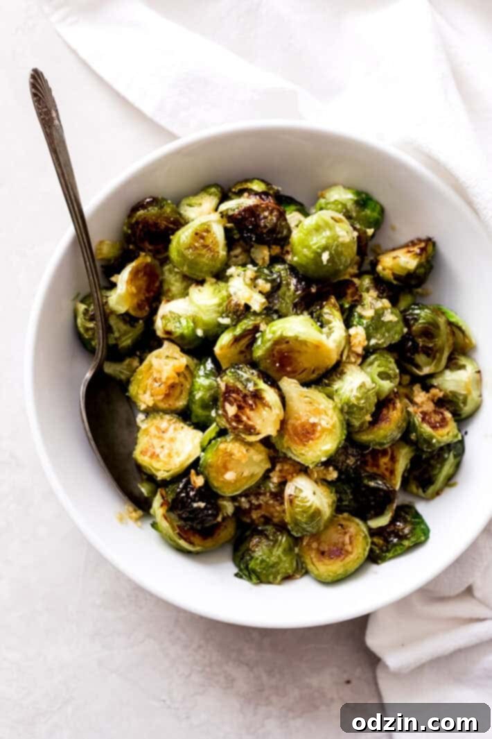 A white bowl brimming with golden-brown garlic butter Brussels sprouts, garnished with fresh herbs, resting on a textured grey surface with a serving spoon.