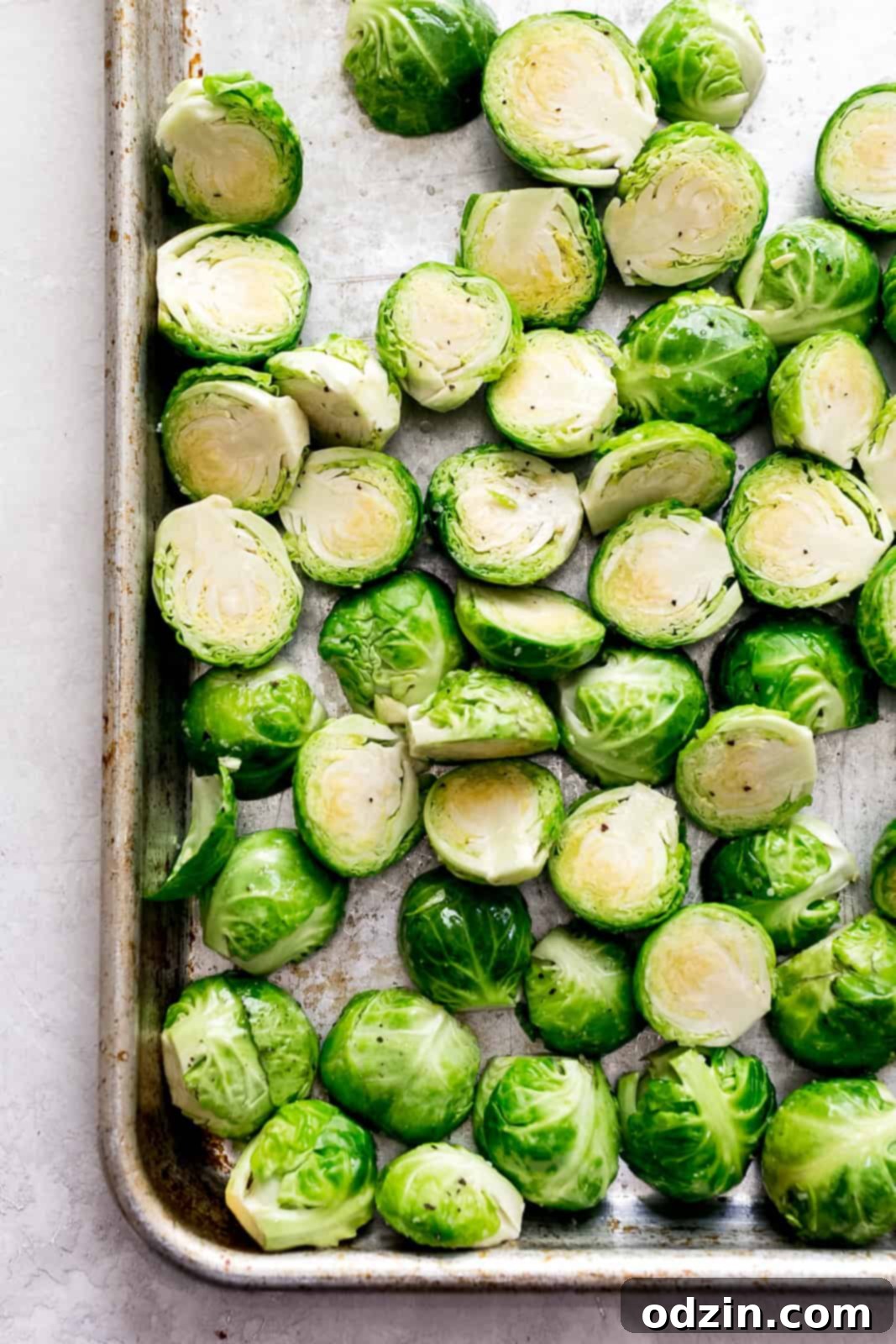 A sheet pan filled with perfectly halved fresh Brussels sprouts, lightly seasoned with salt and pepper, ready for roasting in the oven.