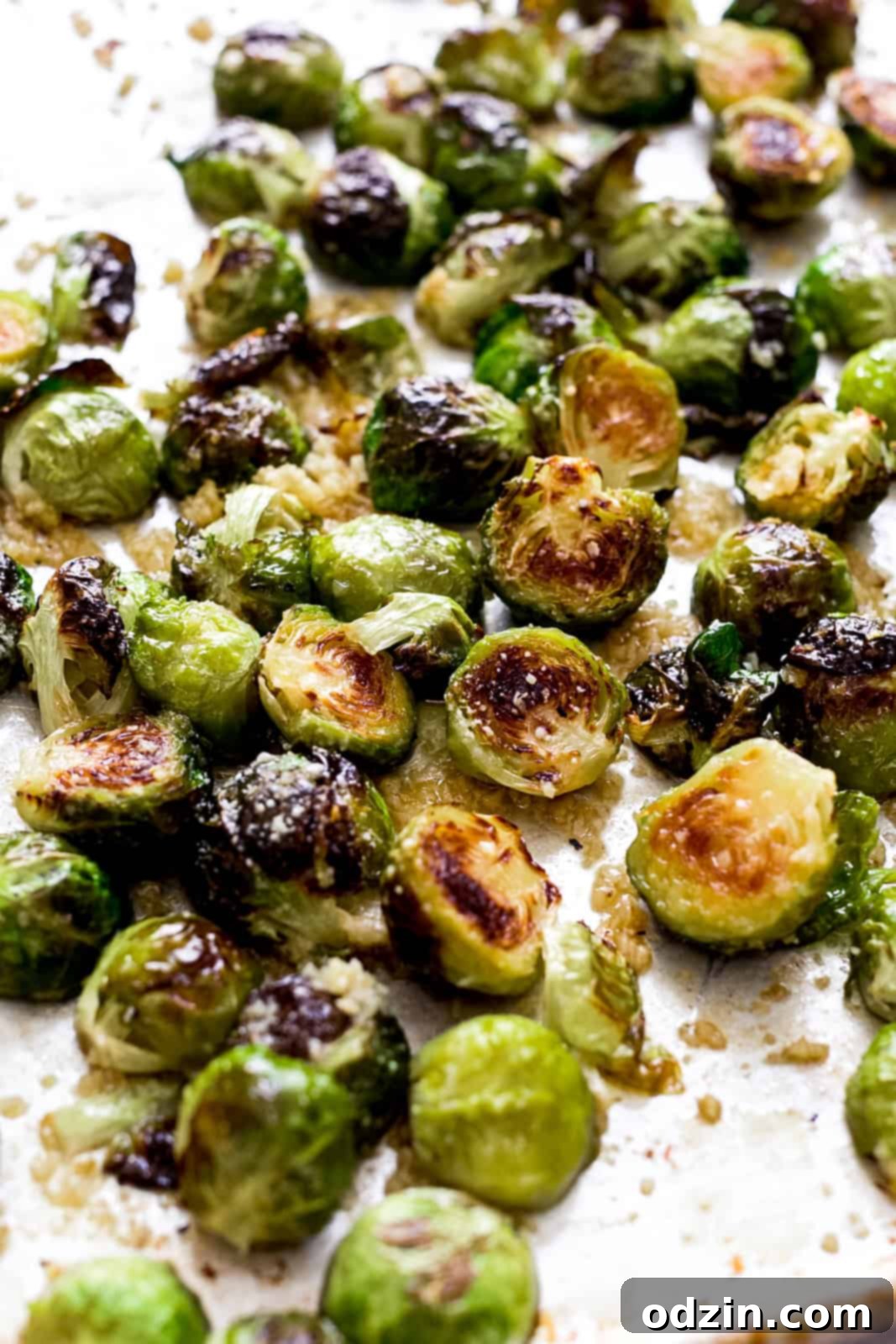 Freshly roasted Brussels sprouts spread across a sheet pan, generously coated in a shimmering garlic butter sauce and sprinkled with grated Parmesan cheese, ready to be served.