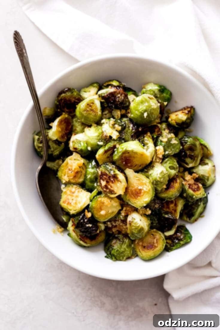 A close-up of a rustic wooden cutting board featuring a large pile of freshly roasted Brussels sprouts, glistening with a savory garlic butter sauce and sprinkled with green herbs.