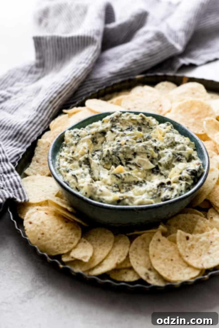 Effortless Slow Cooker Spinach Artichoke Dip 2 Serving dish with tortilla chips and a bowl of prepared slow cooker spinach artichoke dip