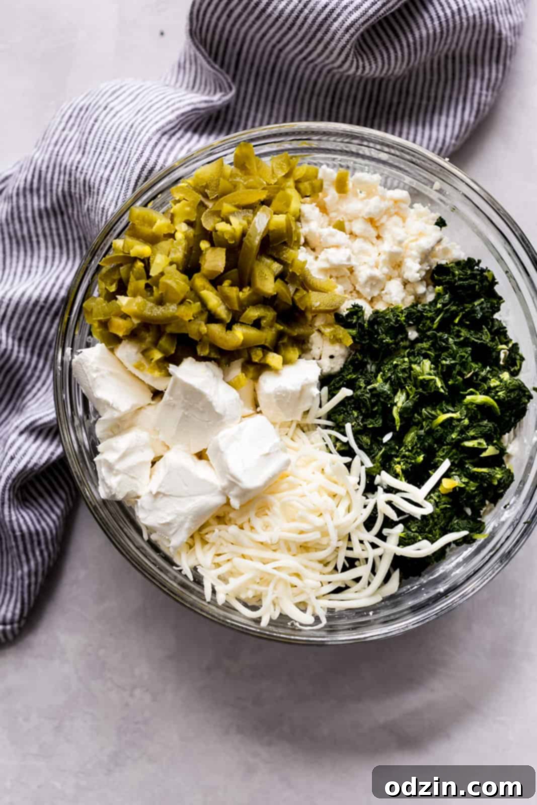 Effortless Slow Cooker Spinach Artichoke Dip 4 Ingredients for spinach artichoke dip in a clear mixing bowl on a grey surface